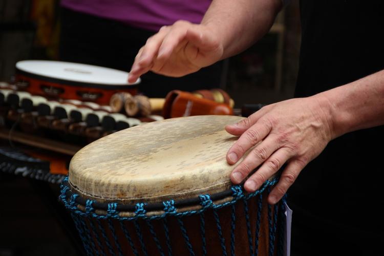 Zwei Hände trommeln, im Hintergrund sind weitere perkussive Instrumente zu sehen.